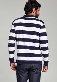 Langærmet polo skjorte i navy og hvide vandrette striber. Har krave og ribbede manchetter. Materialet ser blødt og letvægts ud.
