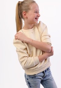 Lichtbeige sweatshirt met poffende mouwen, textuurstof, geribbelde manchetten en een ontspannen pasvorm, gecombineerd met lichtblauwe jeans.