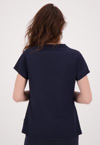 Marineblauwe top met korte mouwen en een ronde halslijn. Glad materiaal, ontspannen pasvorm en subtiele zijsplit accenten. Geen zichtbare patronen of details.