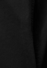 La tela de denim negro presenta un tejido texturizado con un ribete diagonal, exhibiendo una superficie suave y una construcción sólida sin desgastes visibles.