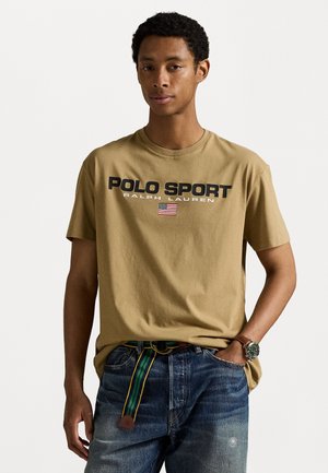 Smilga kokvilnas T-kreklis ar melnu uzrakstu "POLO SPORT", kurā ir attēlota Amerikas karoga ikona. Apvienots ar nolietotām zildiem džinsiem un svītrainu jostu.