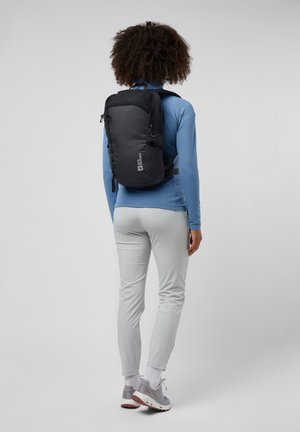 Un sac à dos noir avec une finition texturée, des bretelles ajustables, une poche avant zippée et des compartiments en maille sur les côtés. Porté sur le dos d'une personne.
