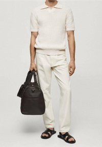 Polo de punto blanco con canalé, pantalones crema, sandalias negras y un bolso de cuero marrón oscuro con asas de mano y hombro.