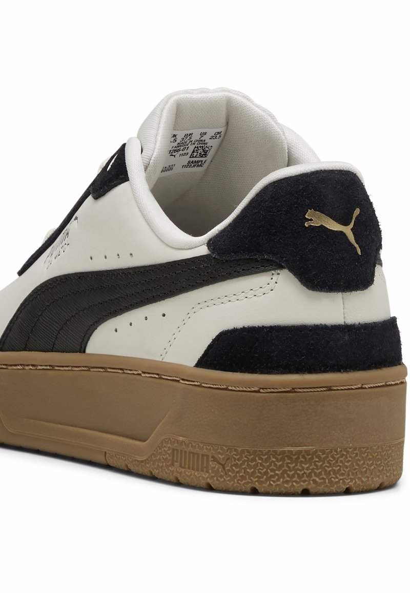 Baskets en cuir blanc avec des accents en daim noir, logo doré et semelle en caoutchouc beige. Présente un col rembourré et des détails perforés sur les côtés.