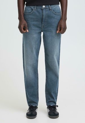 Dżinsy w kolorze wyblakłego niebieskiego, o prostych nogawkach, z pięcioma kieszeniami i zapięciem na guziki. Noszone z czarnymi trampkami.