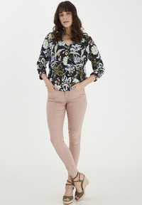 Blumenbluse in Schwarz mit mehrfarbigen Blumen; kombiniert mit rosa Skinny Jeans und grünen Keilsandaletten mit Knöchelriemen.