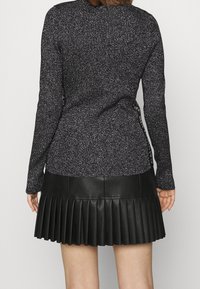 Pull noir en maille avec des paillettes argentées, coupe ajustée et manches longues, associé à une jupe courte plissée en cuir noir.