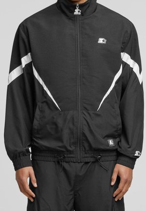 Czarna bluza sportowa na zamek z białymi pasami w kształcie litery V na rękawach i na klatce piersiowej, elastyczne mankiety oraz naszywki z logo gwiazdy na piersi i rękawie.