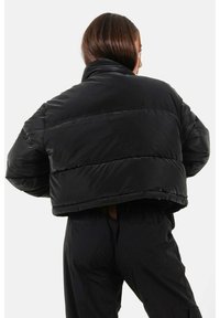 Zwarte pufferjack met een cropped ontwerp, voorzien van een hoge kraag, gequiltte secties en een gladde, glanzende textuur. Subtiele naaddetails.