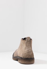 Bottines Chelsea marron en matériau texturé ressemblant à des cheveux, avec une semelle en caoutchouc noir et une boucle discrète à l'arrière pour un enfilage facile.