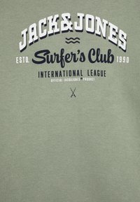 Camiseta de algodón verde con gráficos en blanco y azul marino que dicen "JACK&JONES Surfer's Club" y "LIGA INTERNACIONAL."