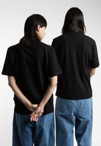 Svarte bomull t-skjorter med korte ermer vist på to personer, kombinert med blå denimbukser. T-skjortene har et enkelt design og passform.