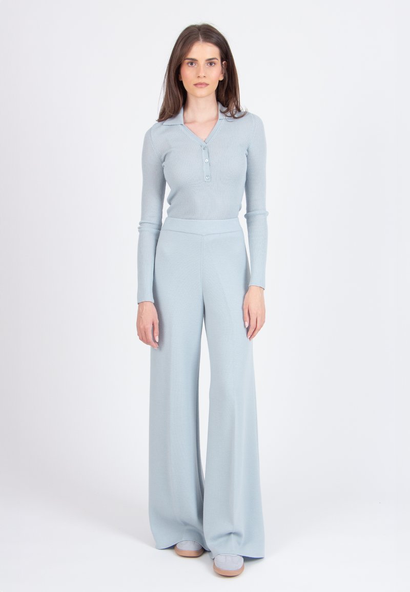 Lichtblauw ribgebreid truitje met een knoopsluiting bij de kraag en lange mouwen, gecombineerd met bijpassende hoge taille wijde broek. Gladde textuur, moderne pasvorm.