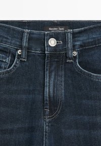 Donker denim jeans met een hoge tailleband, zilveren knoopsluiting en subtiele stikseldetails. Het label vermeldt "Massimo Dutti."