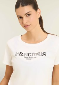Camiseta de algodón blanca con el texto impreso en negro "PRECIOUS Moments FREDDY" en varias tipografías, cuello redondo y mangas cortas.