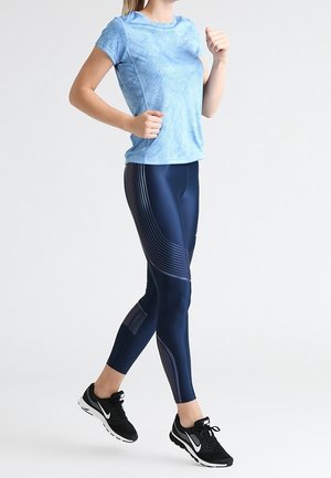 Top deportivo de manga corta azul claro con patrón texturizado, combinado con leggings ajustados color azul marino con detalles de rayas y zapatillas negras.