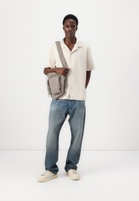 Lys beige kortermet skjorte, lyseblå jeans og kremfargede sneakers. Grå veske med glidedetalj, plassert over kroppen.