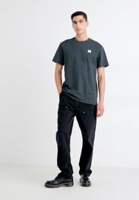 Dark gray cotton t-shirt with short sleeves, featuring a small logo patch. Paired with black denim pants and sturdy black boots.