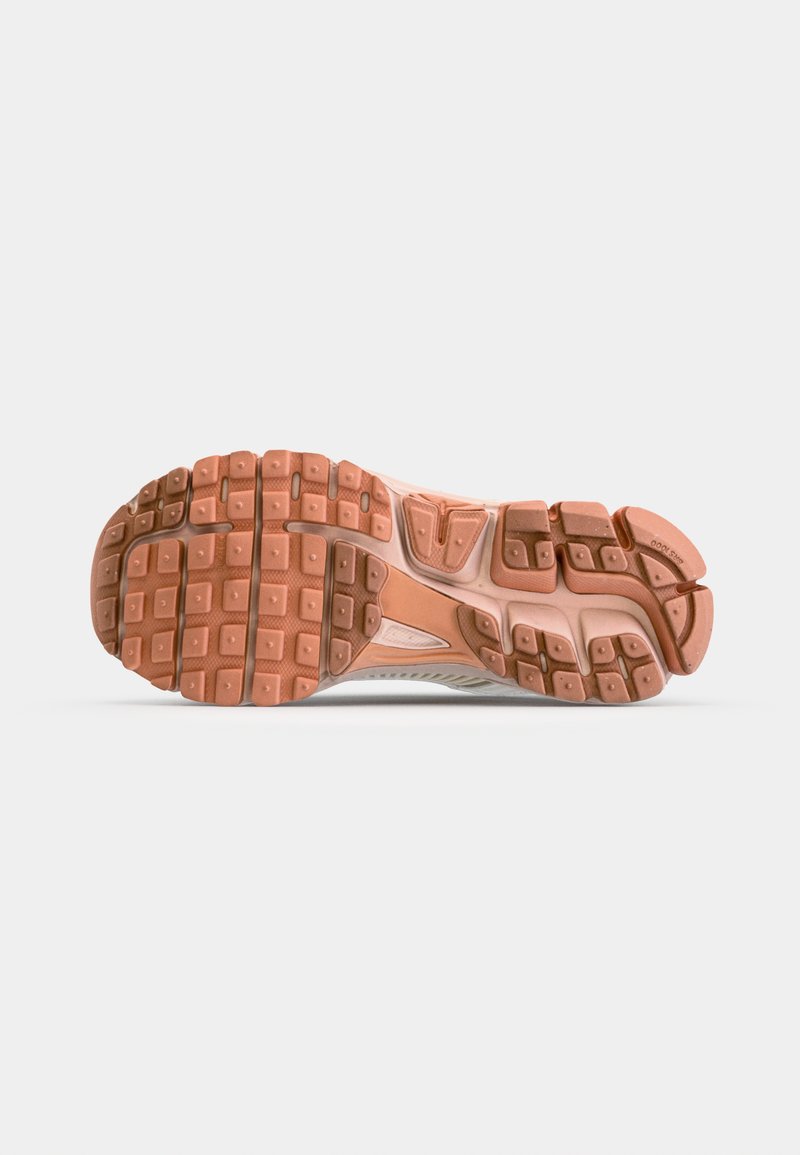 Hardloopschoen zool met een gestructureerd rubberen oppervlak in tinten van bruin en oranje, met een patroon van vierkanten en richels voor grip.