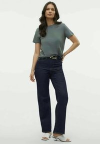 Γκρίζο κοντομάνικο μπλουζάκι συνδυασμένο με σκούρα μπλε ίσια τζιν παντελόνια. Μαύρη ζώνη με χρυσό αγκράφα, λευκά ανοιχτόχρωμα παντοφλέ παπούτσια με τακούνι. Λείες υφές.