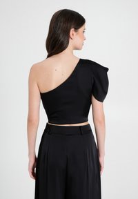 Crop top nero a spalla unica con una manica a sbuffo strutturata, in un satin liscio e dalla vestibilità aderente, abbinato a pantaloni neri a vita alta.