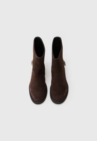 Botas de tobillo de ante marrón con un acabado ligeramente texturizado, que cuentan con una punta redonda, suela plana y un detalle de acento dorado en el lateral.