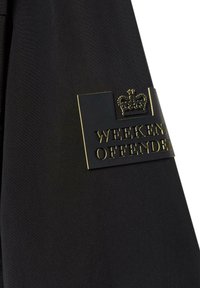 Black fabric with a soft texture, featuring a gold logo plate that reads "WEEKEND OFFENDER" and a crowned emblem above.