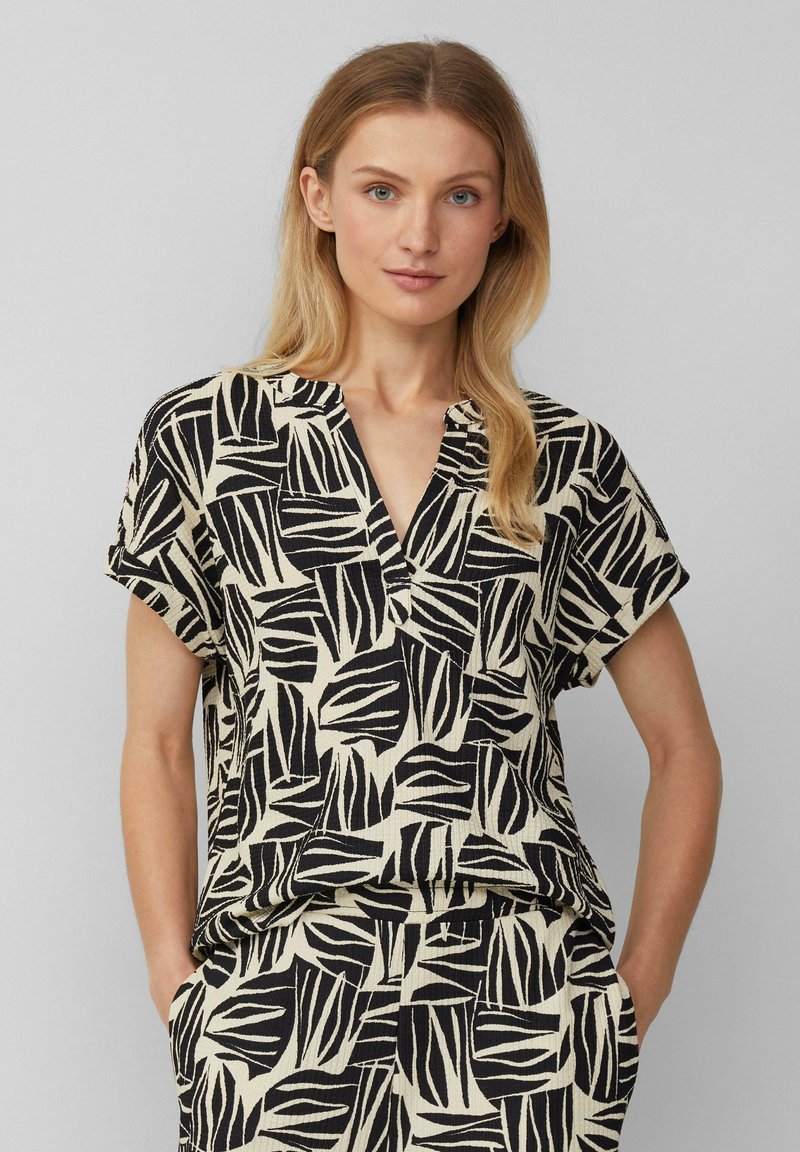 Korte mouw top in beige met een gedurfde zwarte bladpatroon, met een v-halslijn en een comfortabele pasvorm, gemaakt van ademend materiaal.