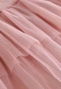 Svetloružový tylový materiál, s jemnými záhybmi a mäkkou, priesvitnou textúrou. Materiál je delikátny a vzdušný, s tečúcim vzhľadom.