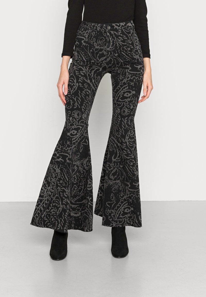 Pantaloni neri a campana con motivo floreale in grigio scuro. Tessuto texturizzato, design a vita alta, orlo rifinito con lieve sfilacciatura. Indossati con stivaletti neri.