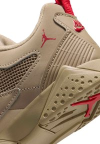 Beige urheiluavaus, jossa on teksturoitu päällinen verkkosysteemeillä, punaisia yksityiskohtia ja kuvioitu kumipohja, jossa on Jumpman-logo.