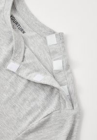 Szara bawełniana koszulka z okrągłym dekoltem, złożonym wykończeniem dekoltu z białymi akcentami z rzepami i luźnym krojem. Prosty, teksturowany materiał.