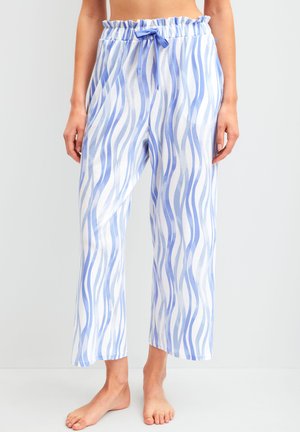 Vrouw draagt losse pyjamabroek tot aan de enkels met blauwe en witte verticale golvende strepen en een elastische tailleband met koord.