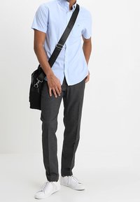 Camisa de botones de manga corta azul claro, pantalones oscuros de textura gris, zapatillas blancas y un bolso mensajero negro. Diseño y colores simples.