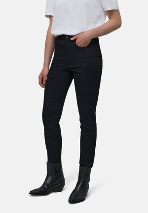 Vaqueros altos negros con un diseño ajustado, hechos de tela de mezclilla. Combinados con botas de vaquero negras con un eje acanalado.
