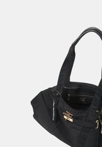 Zwarte nylon draagtas met dubbele handgrepen, een ritsvak, goudkleurige details en een voorvak met klittenbandsluiting. Glad textuur.