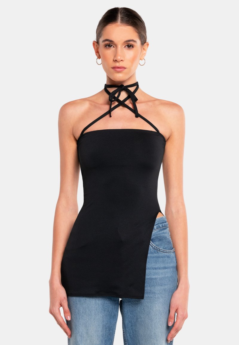 Top halter nero, aderente, con un collo alto e dettagli di cinturini incrociati. Realizzato in un materiale liscio, presenta uno spacco laterale ed è indossato con jeans azzurri chiari.