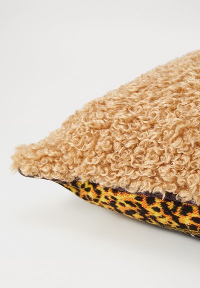 Kwadratowa poduszka z teksturowanym, kręconym beżowym wierzchem i spodem w leopardzi wzór w żółtym i czarnym. Miękki, puszysty materiał kontrastuje z gładk�ą tkaniną.