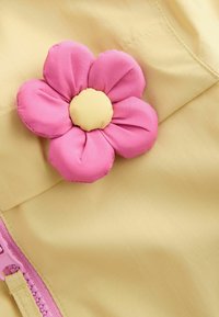 Tela amarilla con una superficie texturizada que presenta una gran flor rosa suave con un centro amarillo y un detalle de cremallera rosa.