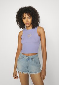 Top cropped em lavanda canelado com um recorte em forma de coração, combinado com calções de ganga azul claro, desbotados, com bordas desfiadas e fecho frontal com botão.