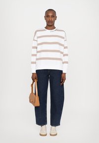Hvit genser med beige horisontale striper, rund hals, løs passform. Kombinert med mørkeblå vide jeans og en lys brun veske.