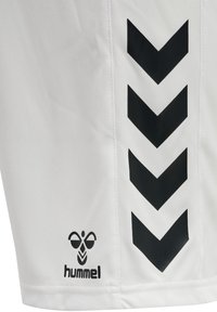 Shorts de sport blancs en tissu lisse, avec des motifs chevron noirs sur le côté et un logo noir près de l'ourlet.