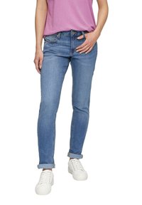 Jeans de mezclilla azul claro con un diseño ajustado, puños enrollados y un estilo clásico de cinco bolsillos, combinados con zapatillas blancas y una camisa rosa.