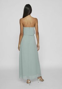 Rochie maxi fără bretele de culoare verde mentă, cu un design stratificat și închidere prin fermoar în spate. Material fin și ușor, cu o siluetă fluidă.