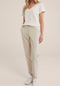 V-ringad randig topp i off-white och beige, i kombination med ljusbeige skräddarsydda byxor och vita sneakers. Platt fram med fickor.