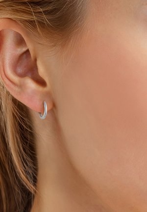 Boucle d'oreille en argent présentée dans l'oreille. Le design est lisse avec une finition polie et une forme circulaire.