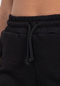 Un pantalon de survêtement noir en tissu texturé, avec une taille élastique et un cordon de serrage réglable à la taille pour un ajustement sûr.