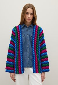 Cárdigan de ganchillo con rayas audaces en rosa, azul, verde y azul oscuro. Presenta un ajuste relajado con mangas anchas y un punto texturizado.