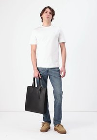 Borsa tote in pelle nera con due manici lunghi, forma rettangolare, texture liscia e design minimalista, tenuta da una persona in abbigliamento casual.