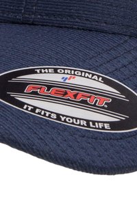 Tumesinine Flexfit müts, millel on tekstureeritud kangas, kõver visor ja ovaalne kleebis punase ja valge tekstiga, kus on kirjas "The Original Flexfit."